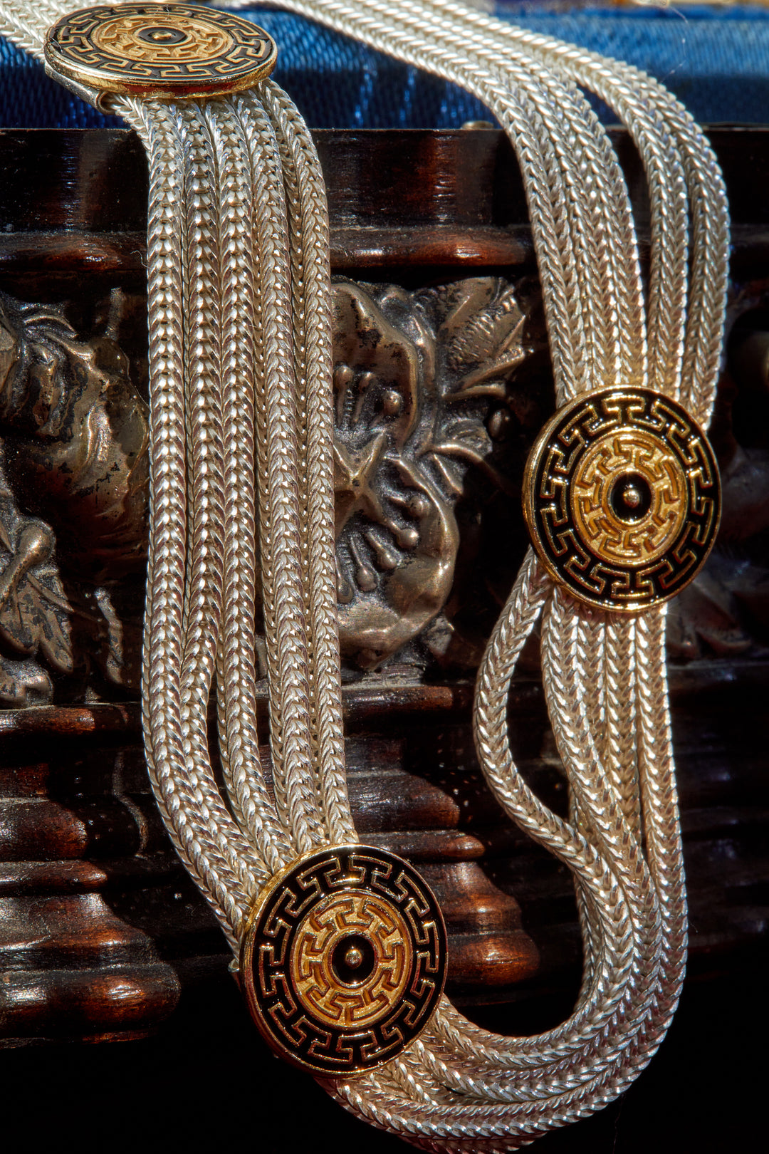 Two silver necklaces with gold circular clasps on a decorative wooden background