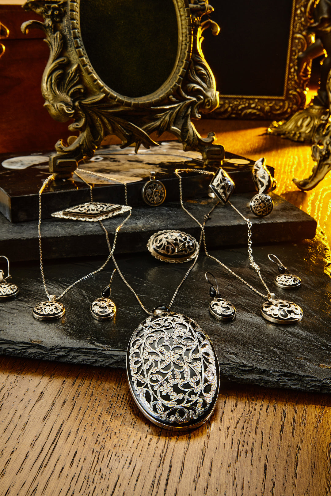 Silver jewelry set including pendants and necklaces on a dark surface with a decorative mirror in the background.