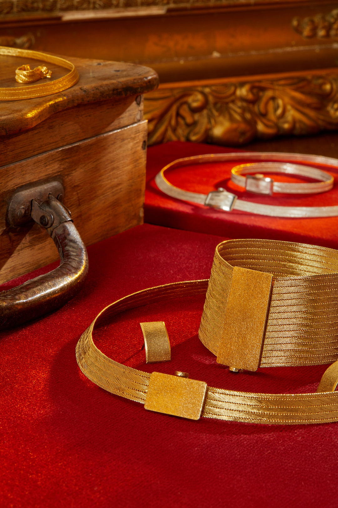 Gold bracelet on a red surface with a wooden box in the background